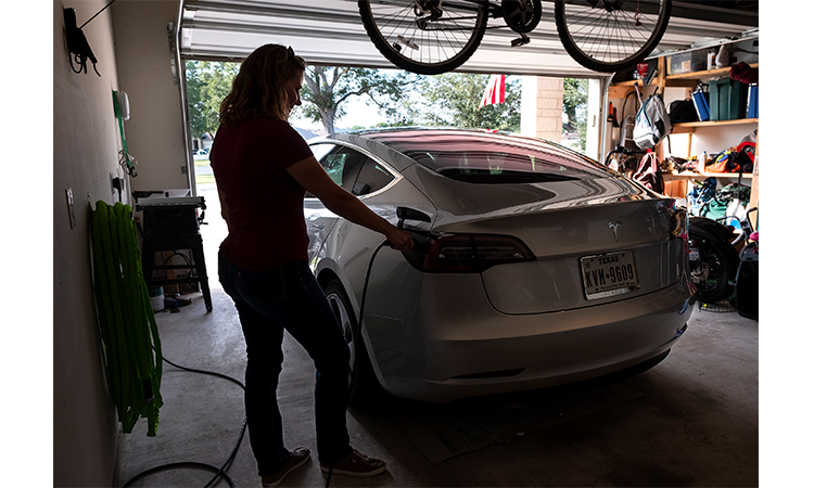 Deanna Bodine plugs a charger into the back of her Model 3 Tesla in the garage of her Bastrop home using a 240-volt outlet, the type typically used for clothes dryers. Bodine says charging the car has little noticeable effect on her monthly power bill. (Laura Skelding photo)